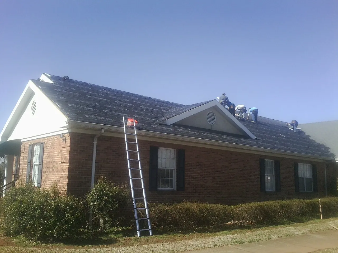 Crew tearing shingles off a brick ranch roof with a ladder set — Metal Roof Repair work by our crew in Belton